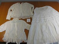 Three items: Two white lace tops and one white petticoat laid flat on a brown surface.