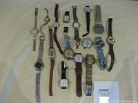 Overview of 16 assorted wristwatches with various bands and styles laid out on a surface.