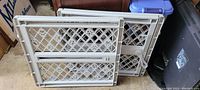 Two white plastic pet gates stacked, showing lattice design and locking handle