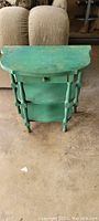 Front view of antique solid wood side table showing one drawer and two lower shelves, green distressed paint with worn areas