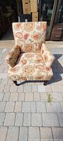 Front view of the patterned fabric armchair on a stone tiled floor, showing the full chair with cushions and armrests.