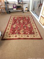 Full view of the Heritage Avery Burgundy area rug laid on a carpeted floor showing design, colors, and condition.