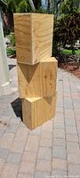 Three plywood wood cubes stacked outdoors on a paved surface, showing the natural wood grain and construction details.