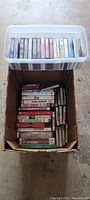 Top-down view of two containers holding music and books on tape cassette tapes in plastic and cardboard boxes.
