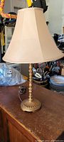 Full view of gold color desk lamp with beige fabric lampshade on wooden surface.