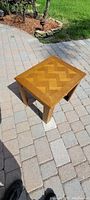 Top view of rectangular oak finish end table with herringbone wood pattern on top, placed outdoors on paving stones.