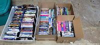 Three boxes filled with mixed DVDs and Blu-Rays, organized in stacks showing multiple cases and box sets including TV series and movie titles.