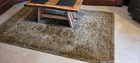Wool throw rug spread on floor under coffee table in living room, showcasing floral and vine pattern in earth tones.