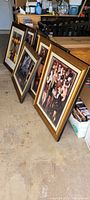 Photograph of multiple gold framed artworks leaned against a surface, showing frames and part of the artworks inside.