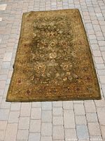 Wool area rug with dark green floral pattern spread out on paved surface, showing full design and colors.