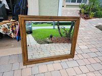Front view of large rectangular mirror with thick wood frame reflecting stone walkway and greenery