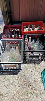 Overview photo showing multiple crates filled with vintage Coca Cola and other assorted glass bottles outdoors.