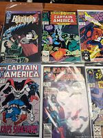 Photo showing Batman, Captain America, Spider-Man comic books with colorful covers and issue details.