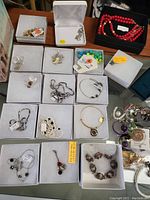Overview of costume jewelry in white boxes on glass surface emphasizing individual boxed items including bracelets, earrings, and necklaces