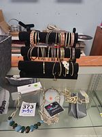 Multiple bracelets and bangles displayed on black velvet jewelry stand alongside necklaces and other jewelry pieces