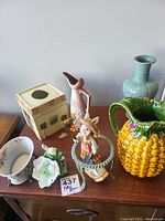 Fall decor items arranged on a wooden table including vase, candle holder, scarecrow figure, pitcher, pineapple-shaped pitcher