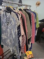 Side view of hanging clothing including floral, polka dot, knit and solid colored shirts and dresses.