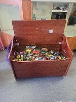 Open wooden chest filled with various toy vehicles and Hot Wheels cars