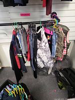 Multiple kids jackets, pants, shorts, and vests hanging on a rack with assorted colors and styles.