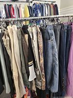 Photo shows multiple pairs of men's pants, shorts, and jeans hanging on racks displaying colors, materials, and styles