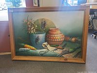 Framed still life painting showing multiple objects including corn, pottery, and a cloth on a surface.