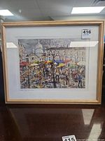 Framed signed Paris Place du Tertre print showing vibrant street scene with umbrellas and Sacré-Cœur in background.
