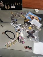 Photo showing religious-themed jewelry including several cross pendants, bracelets, and other religious pendants laid out on a reflective surface.