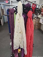 Scarves hanging on a clothing rack featuring white, red, purple, and other colors.