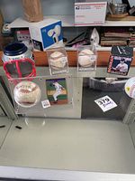 Overview of signed baseballs, displaying multiple autographed balls, baseball card, and Patriots helmet pen holder in display case