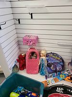 Wide shot showing majority of items including dolls, Elmo plush, Dream Tents packaging, Nerf toy, tennis racket, and green plastic tote.