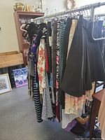 Row of vintage womens dresses, skirts, and tops hanging on metal clothing rack with various prints and colors