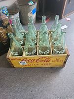 Top-front angle showing all twelve empty vintage Coca-Cola bottles inside the wooden crate with Coca-Cola branding.