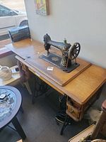 Wide shot of the vintage Singer sewing machine on wooden table with treadle stand and drawers, showcasing full setup.