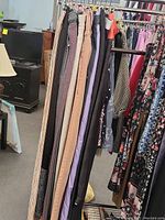 Photo of various women and girls pants on hangers, showing colors such as tan, black, purple, and grey, including studded and casual styles.