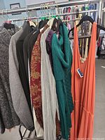 Photo showing a selection of women's and girls' shirts and dresses hanging on a rack including knits, dresses, and cardigans in various colors and patterns.