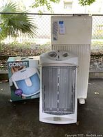 Front view of Holmes heater, Conair foot bath box, and white air purifier against outdoor background with fence and plants.