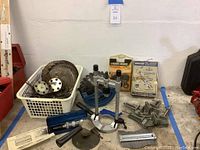 Overview of various tools arranged on the floor including saw blades in a basket, a blue saw blade holder, clamps, and boxed sharpening/grinding accessories.