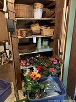 Shelves filled with woven wicker baskets in various shapes and sizes, some stacked and some side-by-side, plus two bins on the floor containing silk flower stems with foam for floral arrangements.