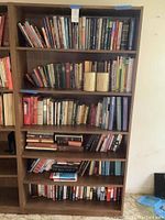 Full view of wooden bookshelf filled with assorted books and two glass candle holders on third shelf from top.