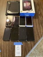 Top-down view of nine devices including smartphones and tablets on wooden surface, showing screen sides and a Tmax tablet box.