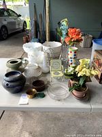 Full view of the table with various decorative vases, pots, artificial flowers, a polka dot cup, and other decor items on a white folding table.