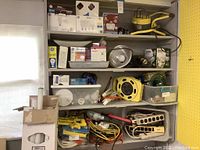 Wide view of shelves containing light bulbs, power strips, extension cords, and work lights.