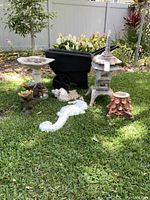 Wide view of the garden decor items arranged on grass showing bird bath, seahorse statue, turtle and rabbit figures, Asian-style lantern ornament, and wheelbarrow in background.