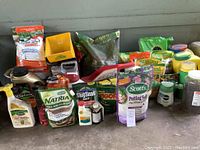 Full lot showing various gardening supplies including bags, bottles, and a spreader on concrete floor.