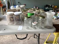 Assorted glass jars including mason jars with metal and plastic lids, two large plastic jars with white lids, and a ribbed glass vase.