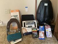 Multiple health and support supplies including an electric neck massager, neck traction device, electric seat and back massager, brace supports in retail boxes and packaging placed on carpet.