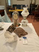 View of the full lot showing clock under dome, two turtle figurines, ceramic doves, and lantern with floral pattern.