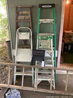 Full view of five ladders and step stool arranged standing against pegboard wall.