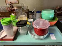 Wide shot of multiple plastic kitchen items including storage containers, bowls, sip cups, and blender bottles grouped on tabletop