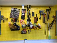 Wide view of various hand tools including gloves, pliers, screwdrivers, gloves, zip ties, utility knife and extension cord on a yellow pegboard.
